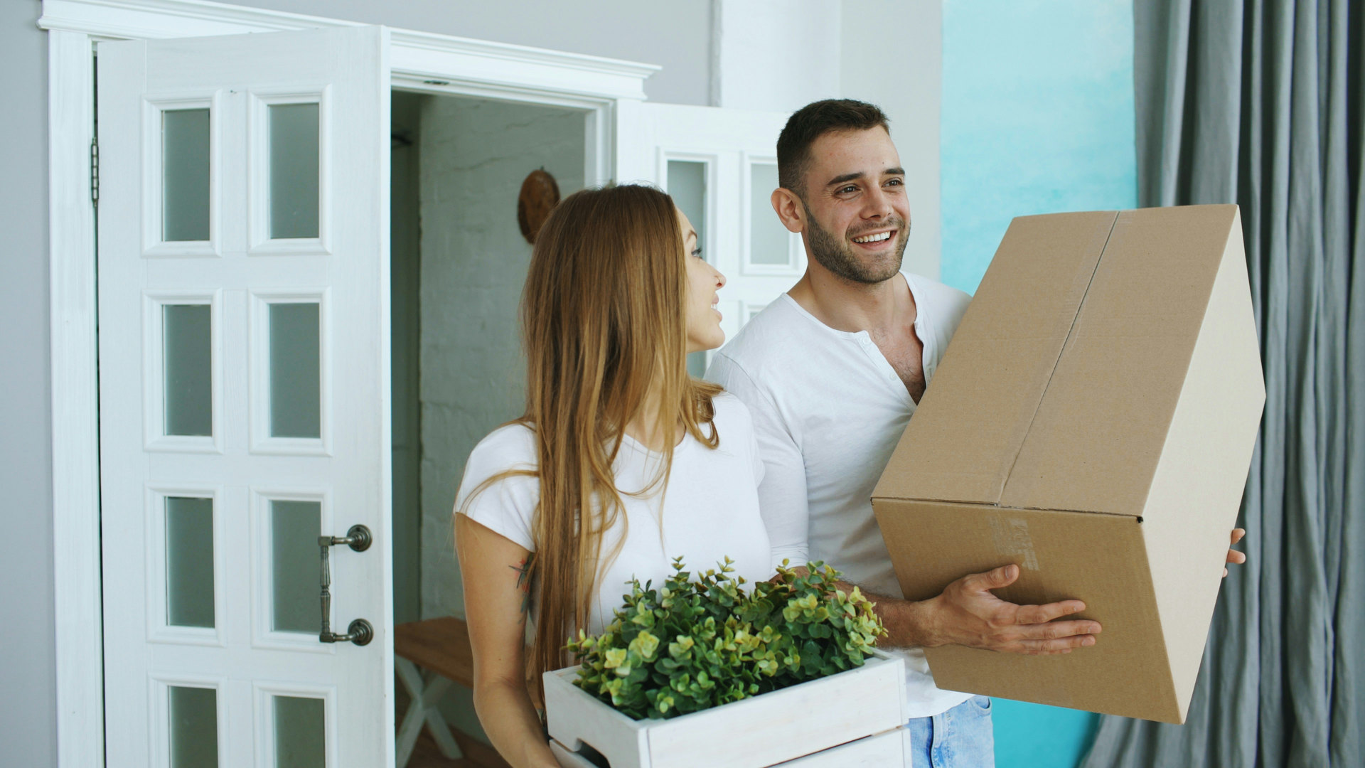 Couple portant un carton de déménagement et une plante dans son nouveau logement